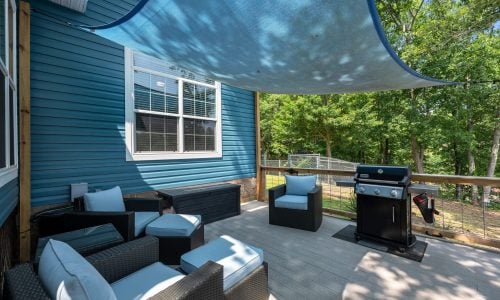 A patio outside a blue house equipped with a grill and outdoor furniture.
